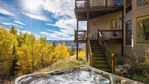 A hot tub with a view of autumn trees and mountains, a wooden deck, and a staircase leading to a balcony. - An Easy 3-Minute Walk to the Slopes! (Steamboat Springs)