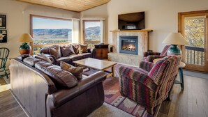 A cozy living room with leather sofas, a fireplace, and large windows offering a view of the mountains. - An Easy 3-Minute Walk to the Slopes! (Steamboat Springs)