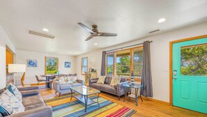 A spacious living room with a sofa, coffee table, and a colorful striped rug. There is a dining area with a table and chairs, and a kitchen in the background.