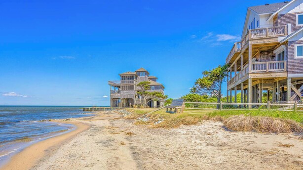 A beachfront property with multiple-story houses, a wooden pier, and a sandy beach.