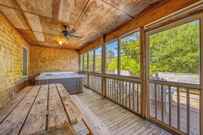 Una terraza de madera con un jacuzzi, un ventilador de techo y ventanas amplias que dan a las copas de los árboles.