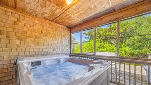 A hot tub in a wooden room with large windows and a view of trees.