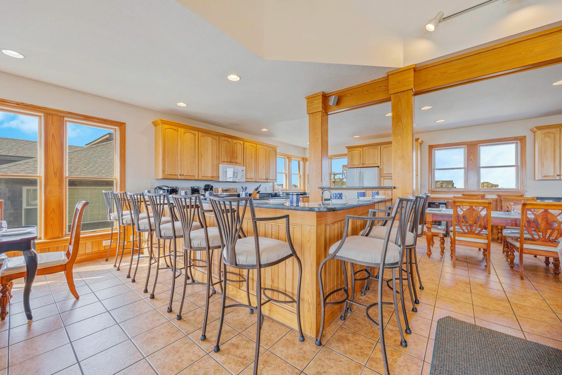 A spacious kitchen with wooden cabinets, a central island with bar stools, and large windows providing natural light.