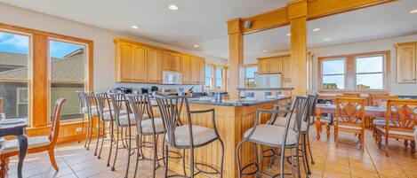 A spacious kitchen with wooden cabinets, a central island with bar stools, and large windows providing natural light.