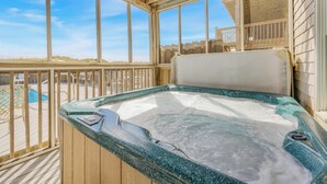 Un bain à remous sur une terrasse en bois, offrant une vue dégagée sur la plage et l’océan.