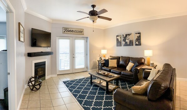 A living room with a fireplace, a ceiling fan, a television, a sofa, a coffee table, and a rug. - Escape to Mountain Escape (Pigeon Forge)