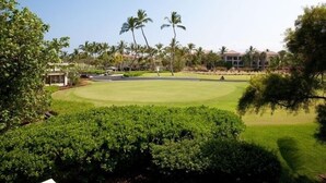 Un campo de golf con un césped bien cuidado, rodeado de palmeras y un edificio al fondo.