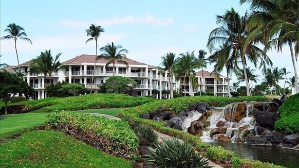 Un resort con un edificio grande, abundante vegetación y una cascada.