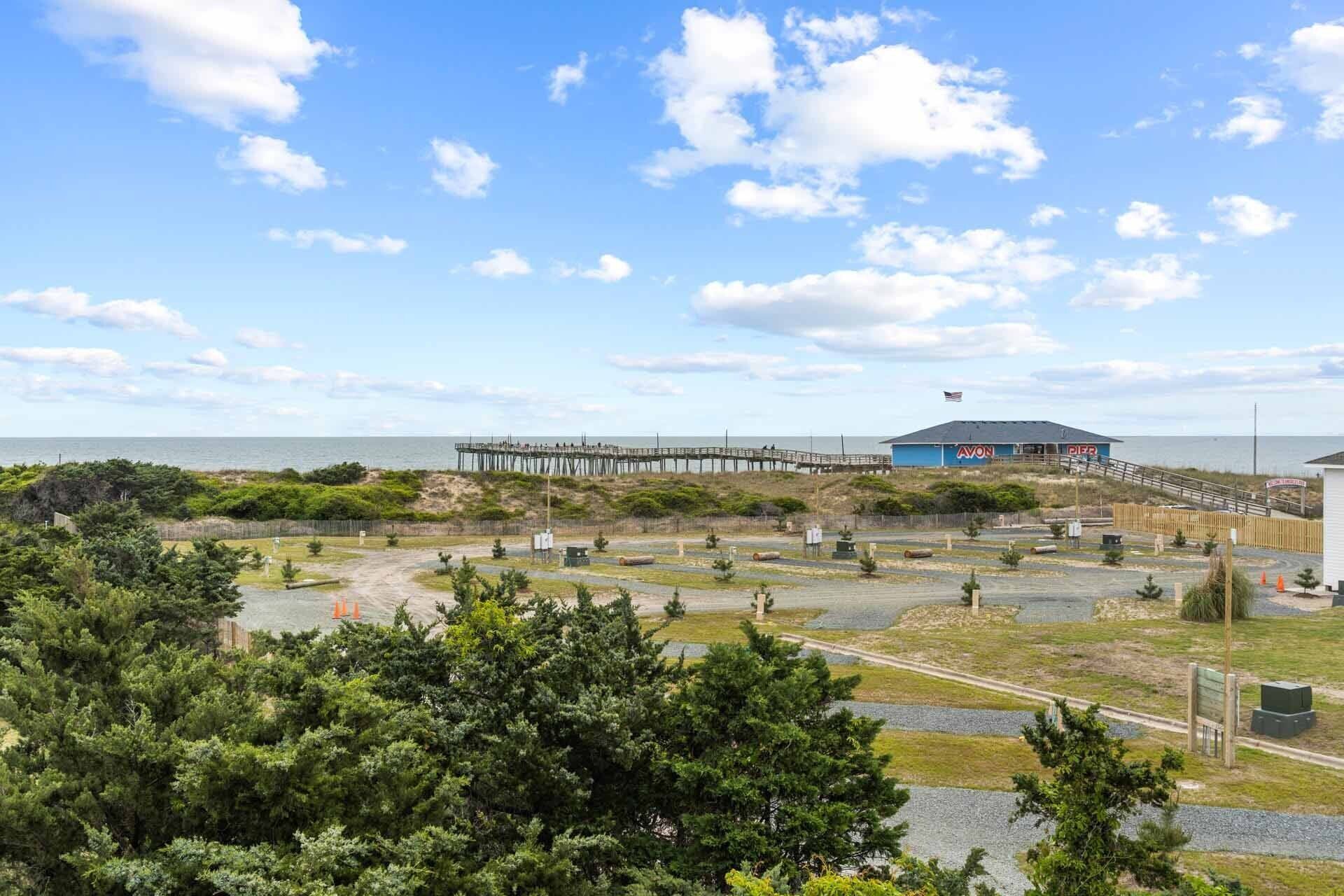 A pier extending into the ocean, a blue building with 'AVON' signage, and a grassy area with trees.