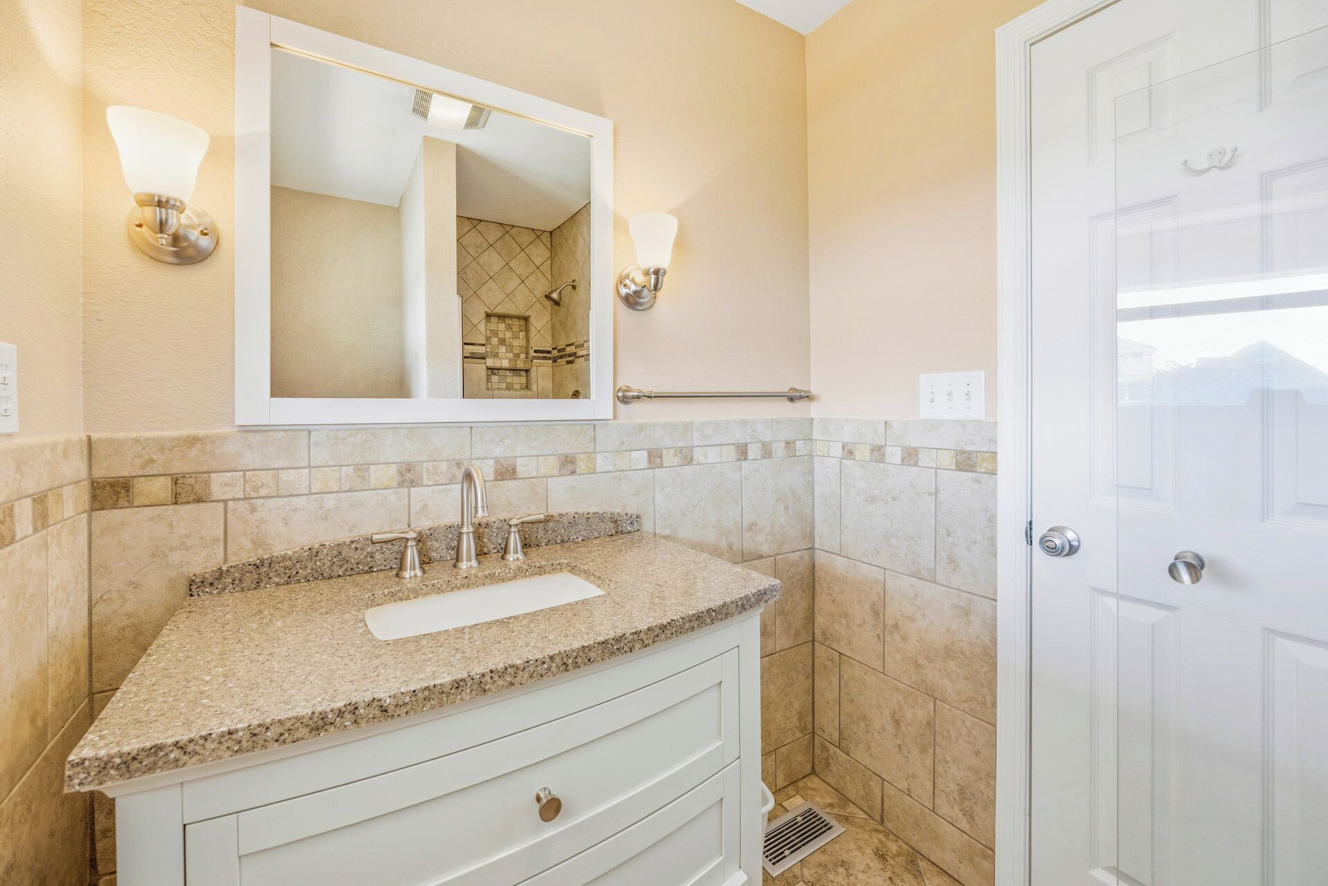 A bathroom with a sink, mirror, towel rack, and door.