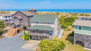 A coastal residential area with houses, a prominent house with a green roof, and a beach in the background. - Oceanfront Avon Home with Private Pool, Hot Tub, Deluxe Game Room, Tiki Bar (Avon)
