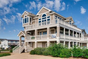 Une maison à plusieurs étages située en bord de mer, dotée d’un balcon, d’un escalier et d’un panneau indiquant qu’elle offre une vue sur la plage.