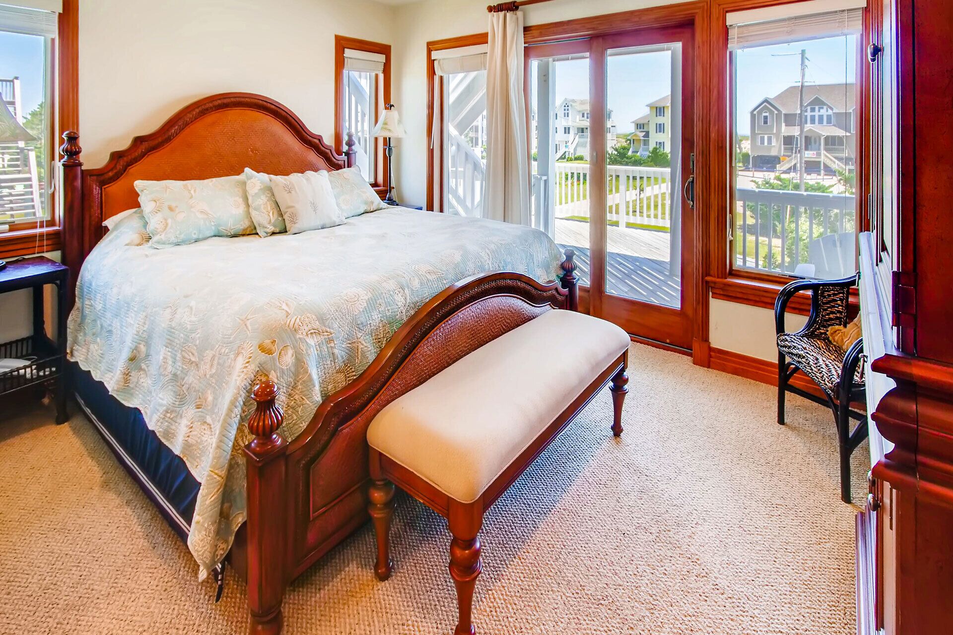 Un dormitorio con una cama grande, un banco, una silla y vistas a una zona residencial a través de amplios ventanales.