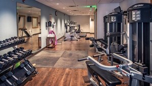 Ein Fitnessstudio mit Cardiogeräten, Gewichten und einer Spiegelwand.