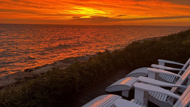 Tramonto sulla costa oceanica, con sedie a sdraio bianche.