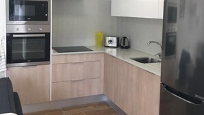 Una cocina moderna con armarios blancos, electrodomésticos de acero inoxidable, microondas integrado, horno y refrigerador.