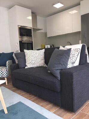 Relax in this stylish living room with a sofa, side table, and chair, surrounded by modern cabinetry and an oven.