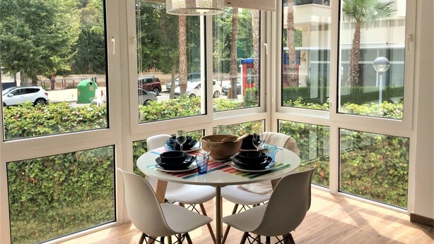 Comedor con una mesa dispuesta para cuatro, ventanas amplias y una lámpara colgante.