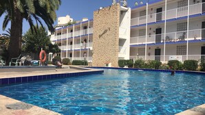 Una piscina con un muro de piedra y un edificio con balcones al fondo.
