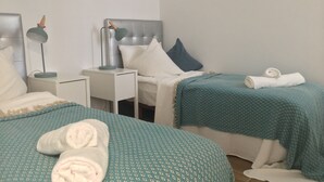 Habitación de hotel con dos camas, una mesita de noche con lámpara y un edredón estampado en azul.