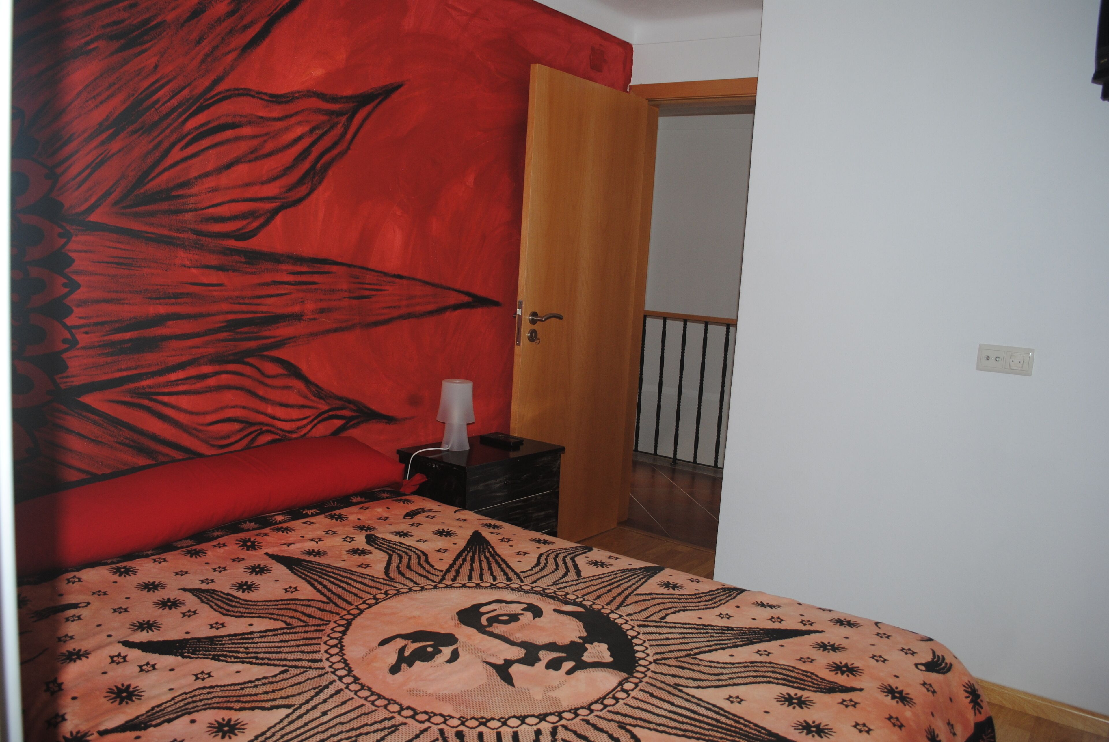 A bedroom with a bed, a nightstand, a red wall, and a door leading to another room.