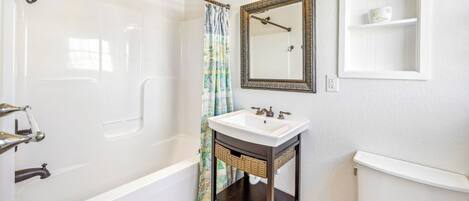 A bathroom with a bathtub, a sink with a mirror above it, and a toilet.