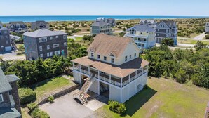 A coastal residential area with multiple houses, including a prominent two-story house with a balcony and a covered porch. - Oceanview Home with Pool, Hot Tub, Game and Media Rooms. I Love Beach Music! (Salvo)