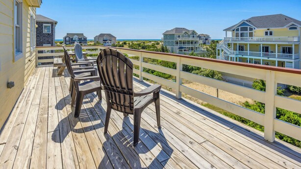A wooden deck with chairs and a table, overlooking a beach and several houses. - Oceanview Home with Pool, Hot Tub, Game and Media Rooms. I Love Beach Music! (Salvo)