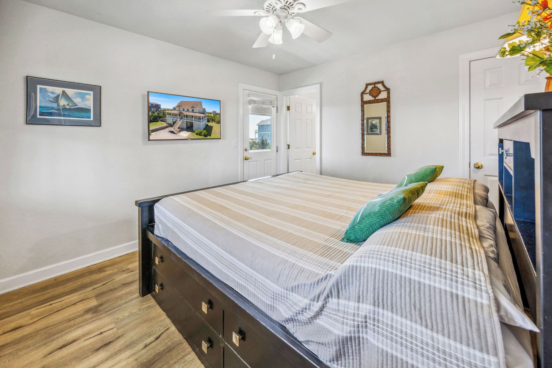 A bedroom with a bed, wooden floor, white walls, and a ceiling fan.