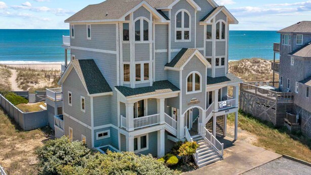 Un'ampia casa a più piani con un balcone e un portico, situata vicino a una spiaggia e con vista sull'oceano.