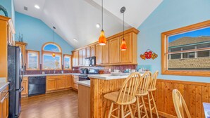 A kitchen with wooden cabinets, a refrigerator, a stove, and a bar area with stools. - Semi-Oceanfront Home w/ Pool, Hot Tub, Elevator, Game Room, Home Theater (Avon)