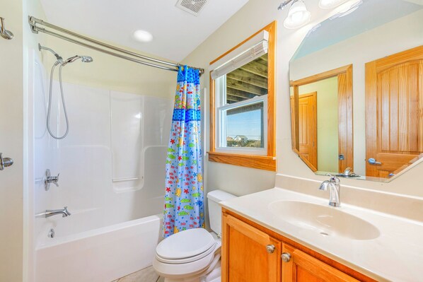 A bathroom with a shower, toilet, and sink, featuring a window and wooden cabinets.