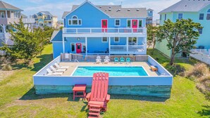 A two-story house with a pool, a red slide, and a deck with chairs. - Semi-Oceanfront Home w/ Pool, Hot Tub, Elevator, Game Room, Home Theater (Avon)