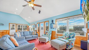 A spacious living room with a ceiling fan, large windows, and a view of the outside. - Semi-Oceanfront Home w/ Pool, Hot Tub, Elevator, Game Room, Home Theater (Avon)