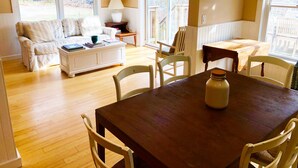 A cozy living room with a wooden dining table, white chairs, a sofa, and a coffee table.