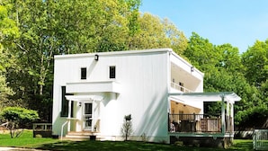 A two-story white building with a covered porch and a small garden area.