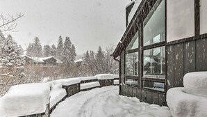 Een gebouw met een sneeuwdak, grote ramen, een houten terras en een besneeerd landschap op de achtergrond.