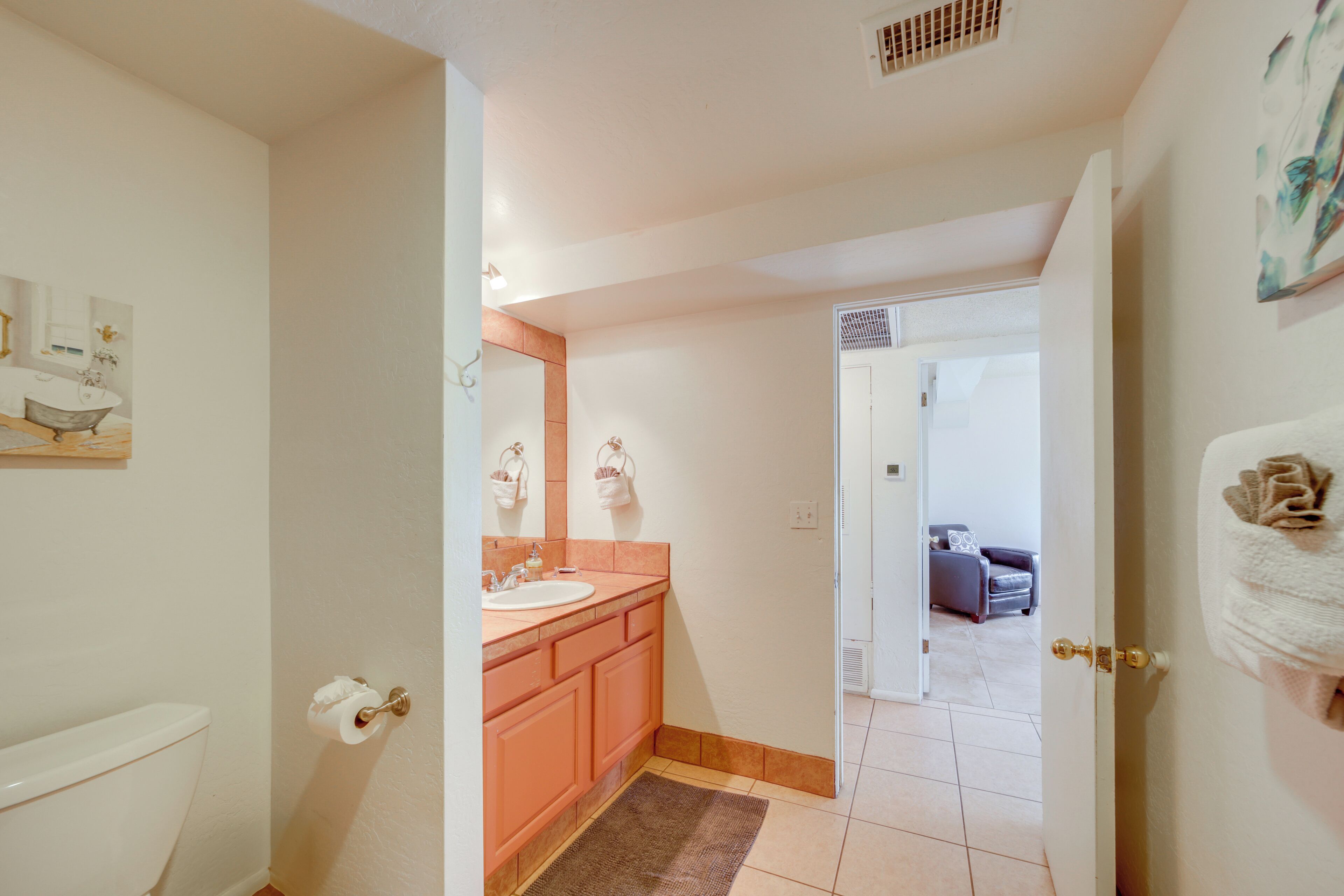A bathroom with a toilet, sink, and mirror. There is a rug on the floor and a towel hanging on the wall.