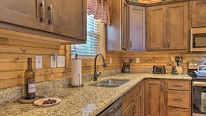 Cucina con mobili in legno, piani di lavoro in granito, lavello in acciaio inossidabile, una bottiglia di vino e un tostapane.