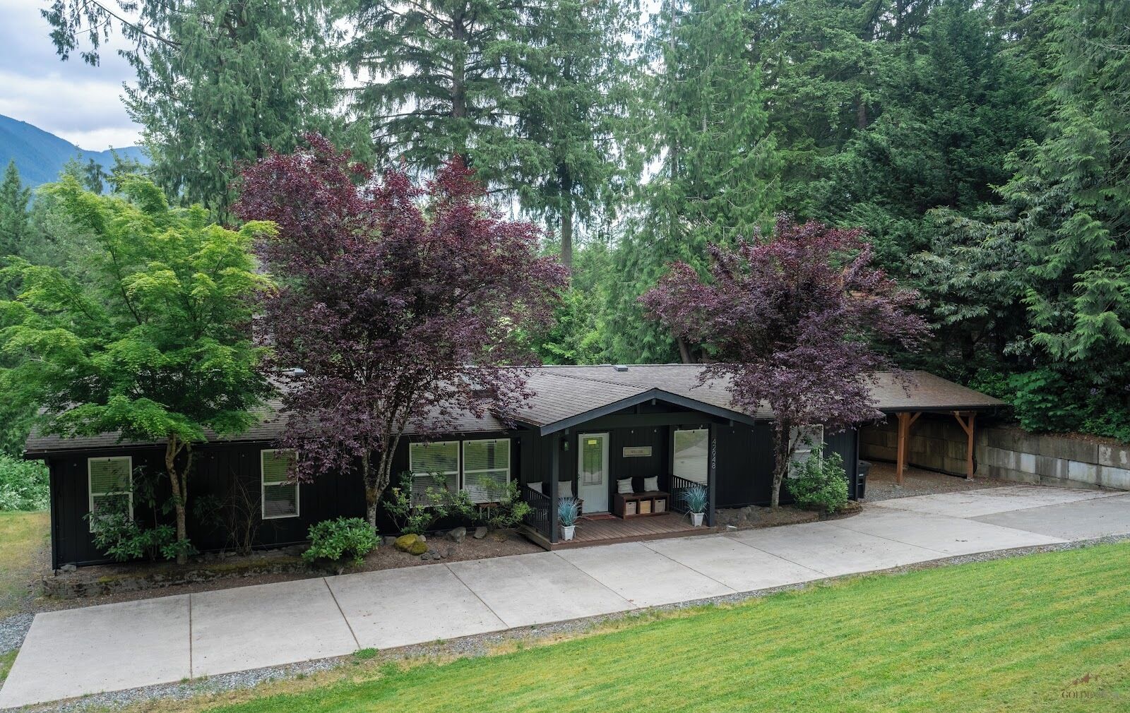 A black single-story house with a porch, surrounded by trees and a grassy yard.