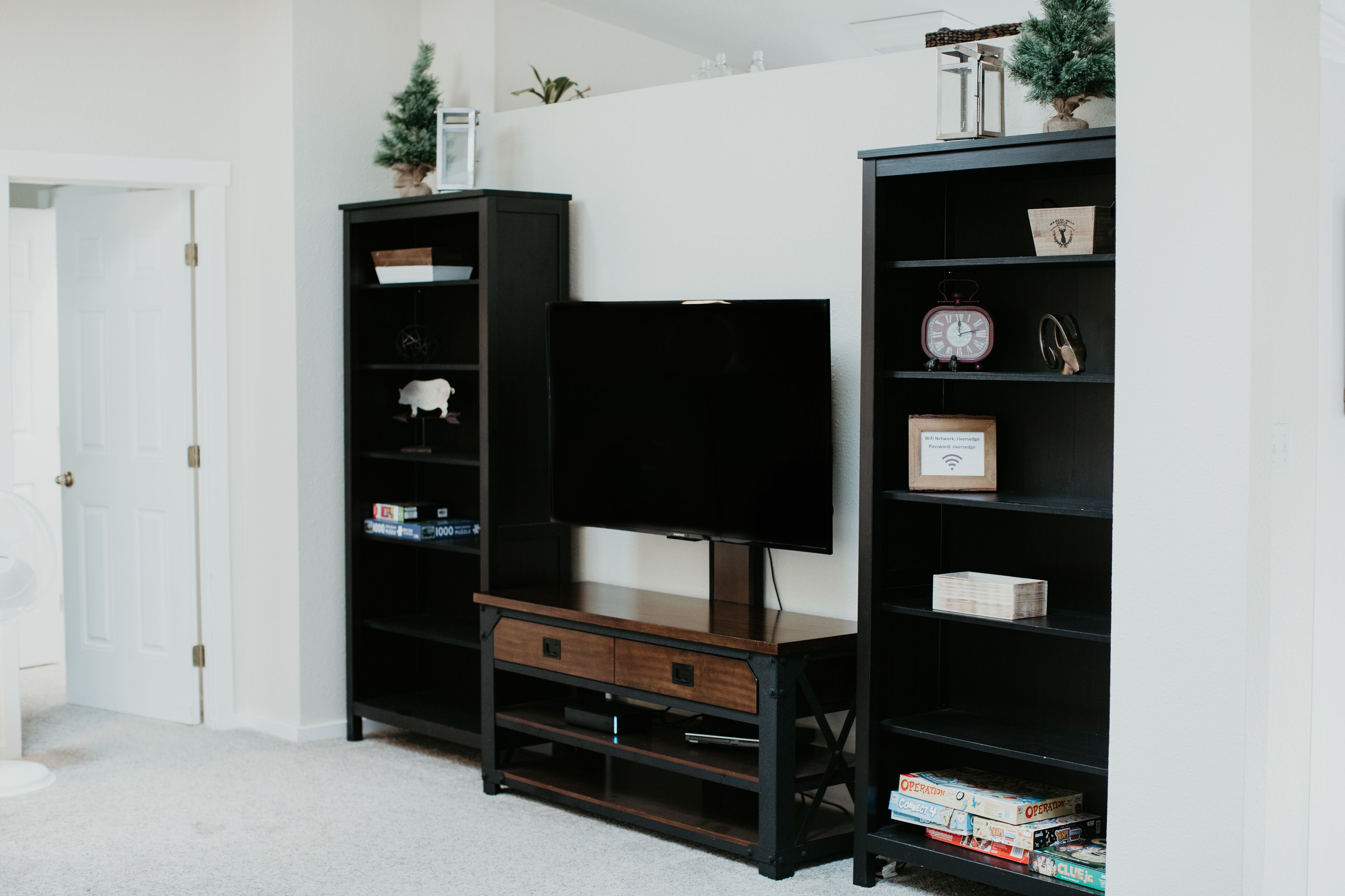 A room with a TV on a wooden stand, surrounded by black shelving units with various items.
