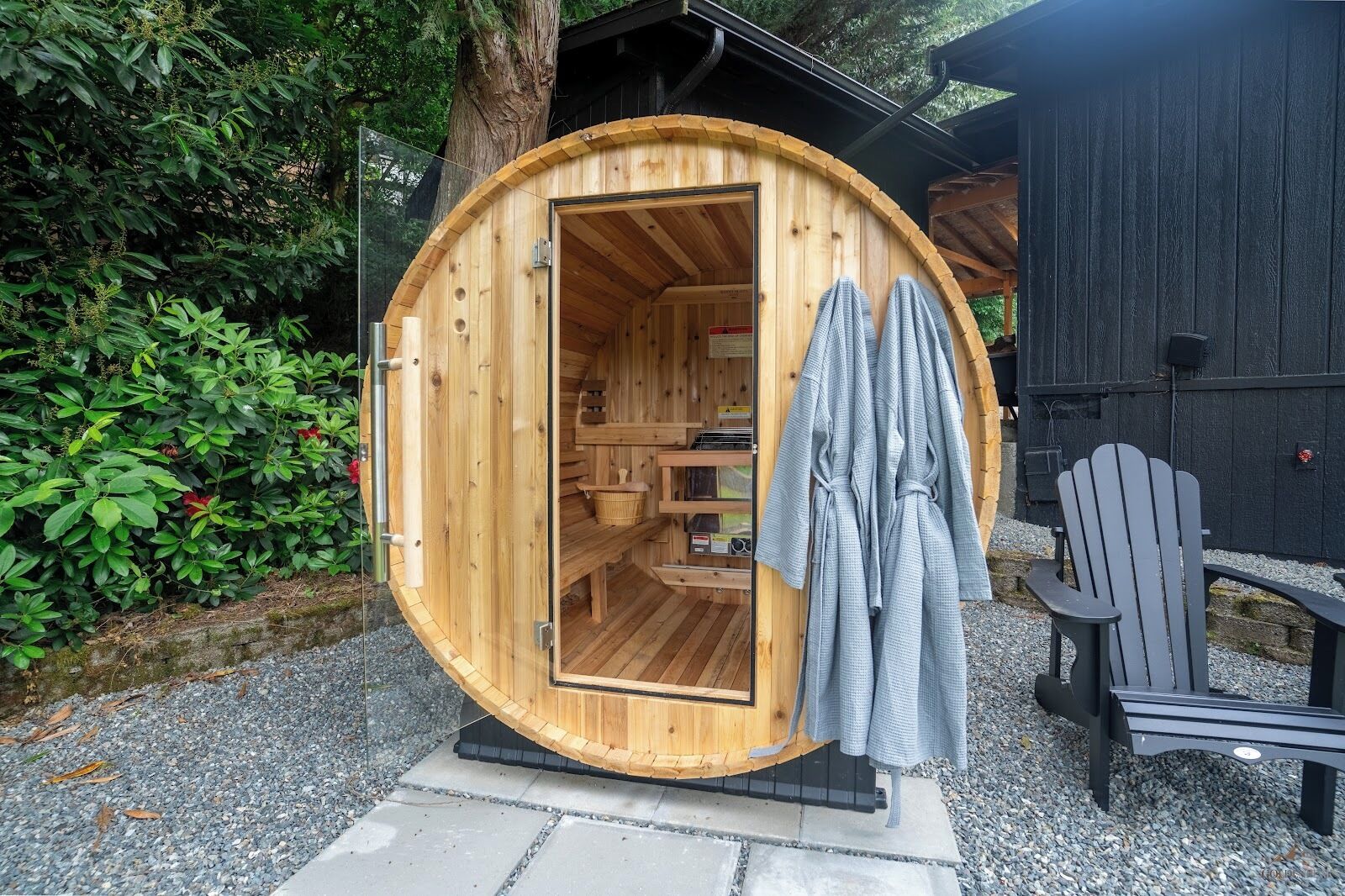 A wooden sauna with a bench inside, a towel hanging on the door, and a chair outside.