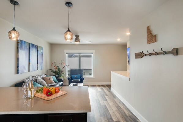 A modern kitchen with a wooden island, pendant lights, and a dining area with a blue chair. - Downtown location, close to Lake, restaurants, and bars! (Sandpoint)