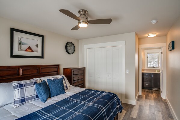 A bedroom with a bed, a ceiling fan, a dresser, a wardrobe, and a view into the kitchen. - Downtown location, close to Lake, restaurants, and bars! (Sandpoint)