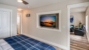 Camera da letto con un letto, una ventola a soffitto, una TV montata a parete e una porta che dà su un'altra stanza.