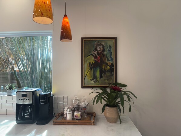 A kitchen with a coffee machine, a tray with jars, a potted plant, and a painting on the wall.