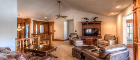 A spacious living room with leather sofas, a wooden entertainment center, and a ceiling fan.