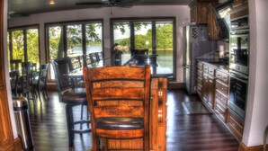 Una cocina amplia con una isla grande, armarios de madera y vistas a un lago a través de ventanales.