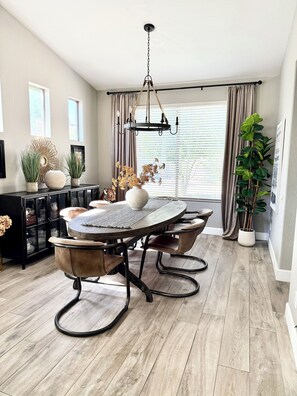 A dining area with a round table, chairs, a chandelier, and a potted plant.