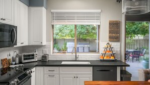 A modern kitchen with white cabinets, a black countertop, a built-in oven, a microwave, and a window with blinds. - Gorgeous Custom Home, Resort Amenities, Heated Pool, Stay in Luxury (Tempe)
